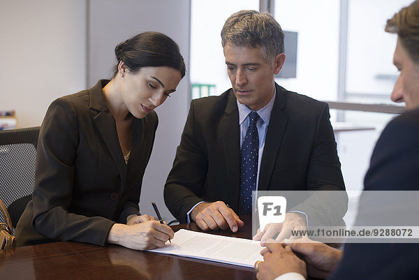 Geschäftstreffen  Geschäftsfrau unterschreibt Dokument  während Mitarbeiter beobachten