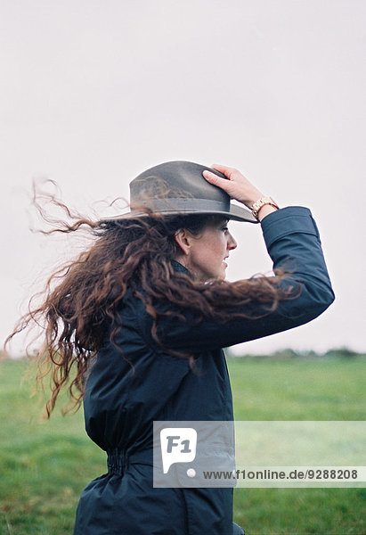 Eine Frau mit langen Haaren  die von der Brise geweht wird und ihren Hut hält.