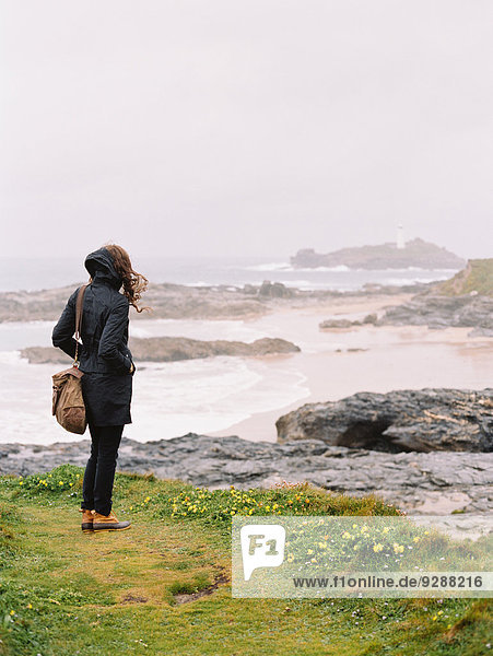 Eine Frau  die an einem windigen Tag am Meer über die Felsen und die Küstenlinie schaut.