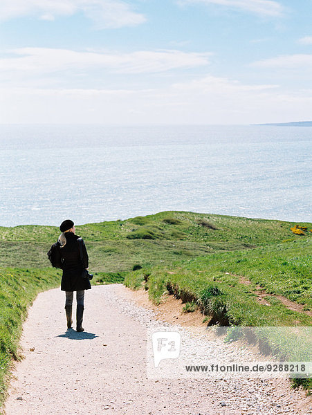 A woman standing on a cliff path looking out at the sea.