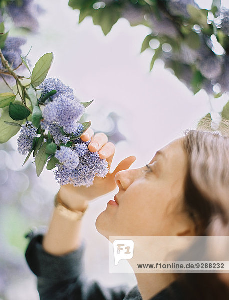 Eine Frau zieht blaue Blumen zu sich heran  um den Duft einzuatmen.