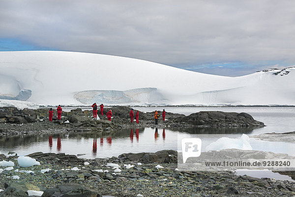 Travellers in bright orange waterproofs observing and photographing the scenery and wildlife on an Antarctic island.