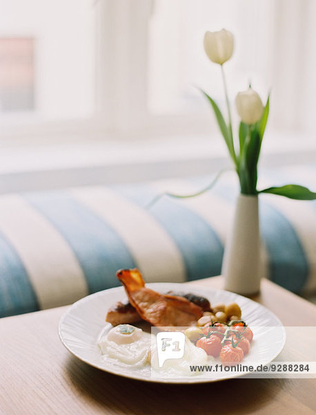 Ein Teller Speck und Eier  ein vollwertiges englisches Frühstück auf dem Tisch. Eine Vase mit weißen Tulpen.