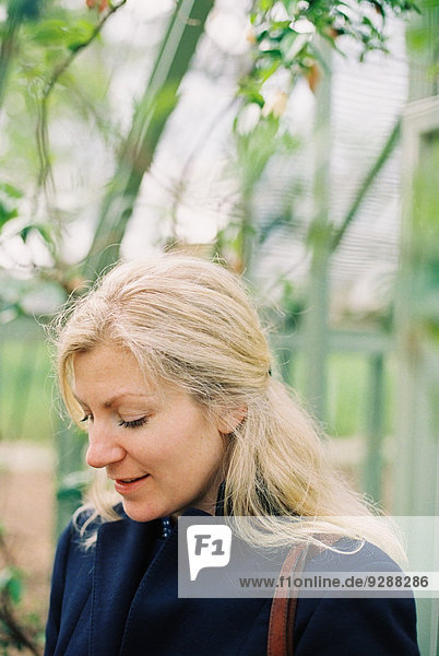 Eine blondhaarige Frau in einem Wintergarten oder tropischen Pflanzenhaus.