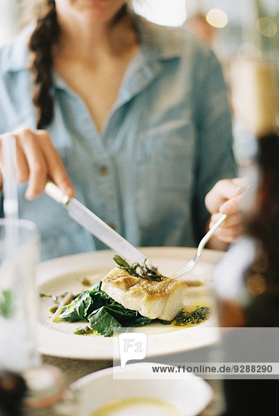 Eine Frau isst eine Mahlzeit  ein Gericht mit Fisch und grünem Gemüse.