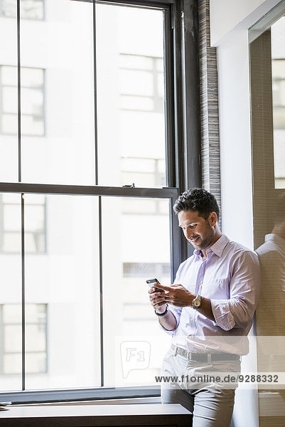Büroalltag. Ein Mann in einem Büro  der sein Smartphone überprüft.