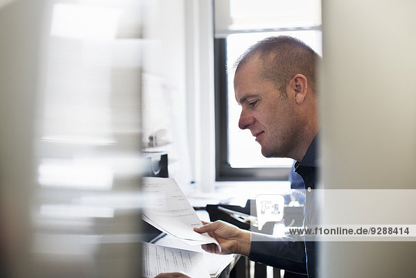 Ein Mann  der in einem Büro arbeitet und Papierkram liest.