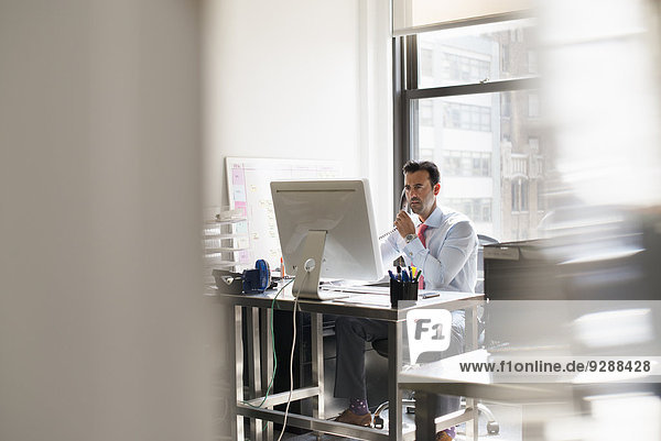 Ein Mann  der an einem Schreibtisch in einem Büro sitzt und einen Computer benutzt.