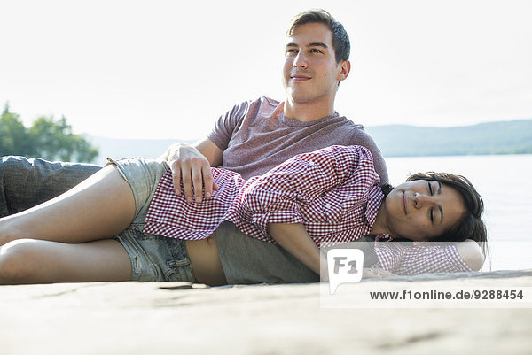 A couple relaxing  lying on a wooden jetty by a lake in summer.