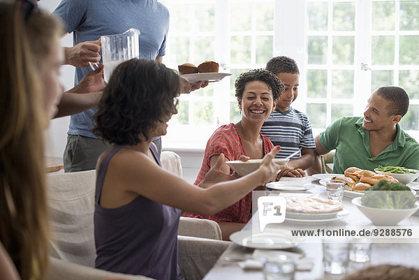Ein Familientreffen  bei dem Männer  Frauen und Kinder an einem Esstisch sitzen und gemeinsam essen.