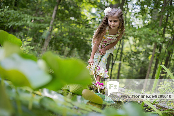 A girl playing at a pond in a forest.
