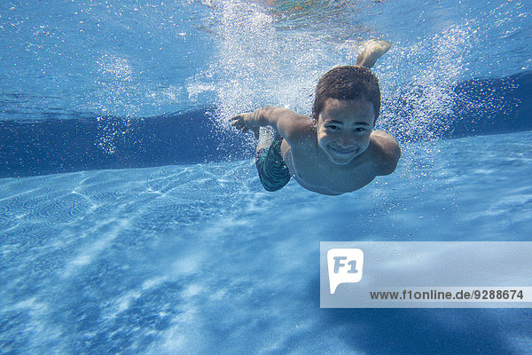 A boy swimming underwater smiling at the camera.