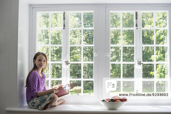 Girl sitting by a window  reading a book.