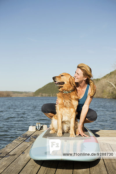 Eine Frau und ein Apportierhund auf einem Paddelbrett auf dem Steg.