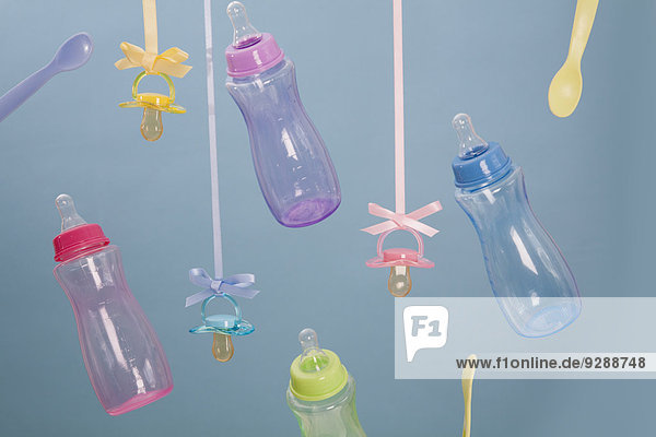 Babyflaschen,  Babylöffel und Schnuller hängen an Bändern.