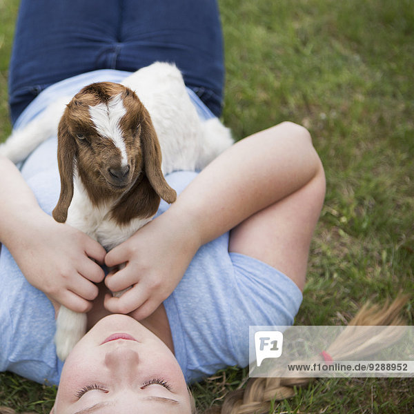 A girl cuddling a baby goat lying on her chest.