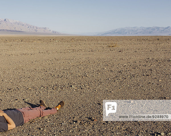A man lying on his back on the ground in the desert.