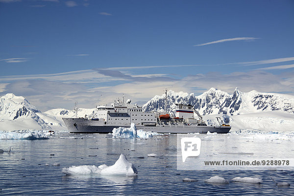 Ein antarktisches Kreuzfahrtschiff mit aufblasbaren Zodiacs auf dem ruhigen Wasser zwischen Eisschollen und Gebirgslandschaft.
