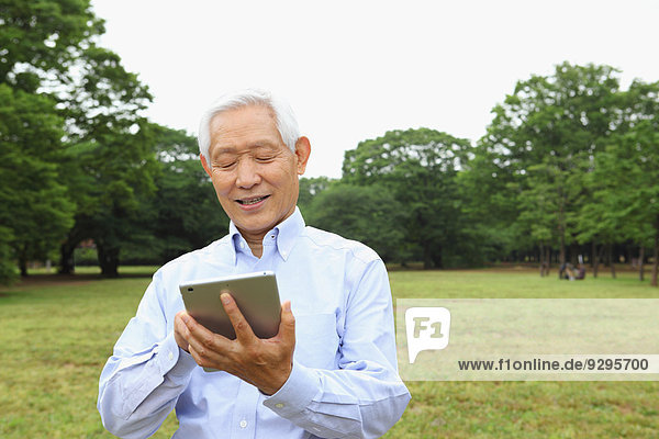 Senior adult Japanese man with tablet in a park