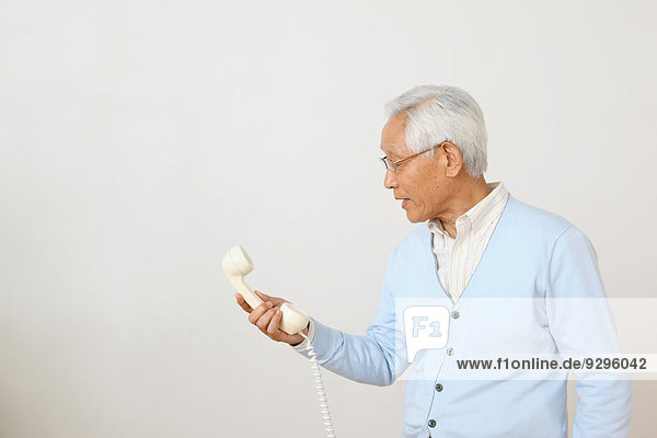 Senior adult Japanese man with phone against white wall