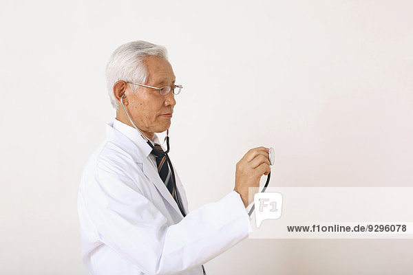 Senior adult Japanese doctor against white wall