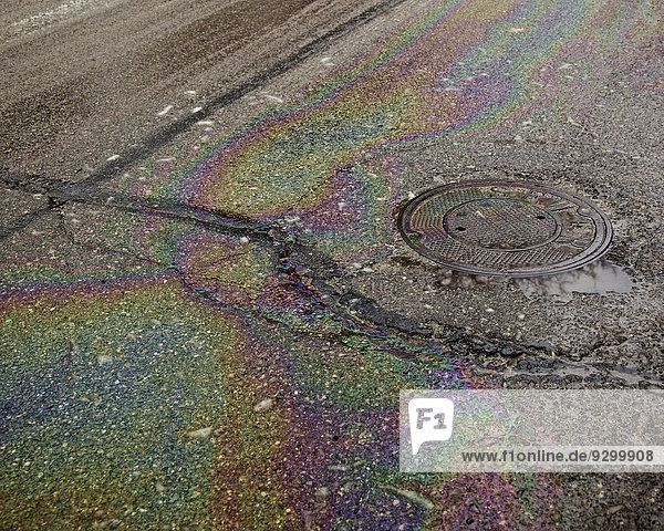 Öl auf einer nassen  gerissenen Straße in der Nähe eines Schachtes