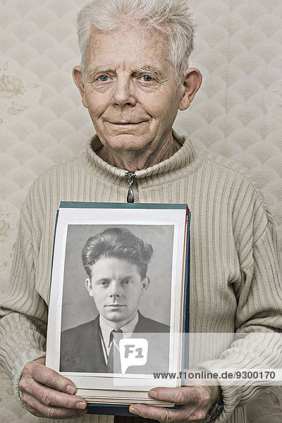 Porträt eines glücklichen älteren Mannes mit einem Bild von sich selbst in den Zwanzigern.
