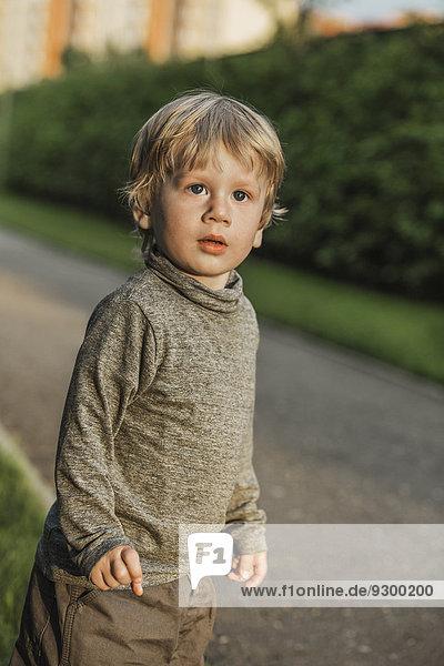 Cute boy looking away while standing on footpath