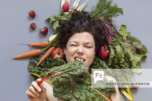 Porträt einer Frau umgeben von Gemüse beißendem Rhabarberblatt auf grauem Grund