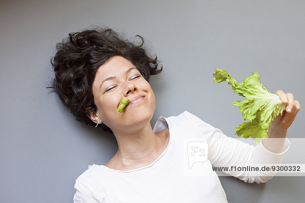 Lächelnde Frau isst Salat über grauem Hintergrund