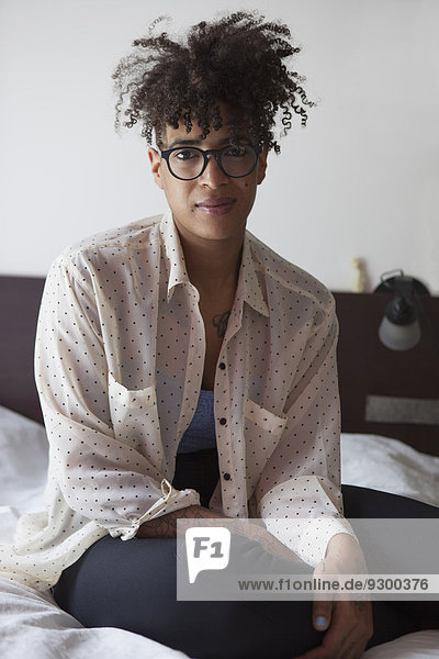 Porträt einer selbstbewussten Frau mit lockigem Haar  die zu Hause auf dem Bett sitzt.