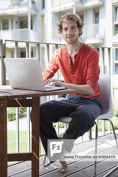 Portrait des jungen Mannes mit Laptop auf der Veranda