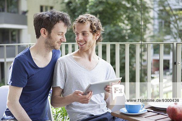 Junges schwules Paar mit digitalem Tablett auf der Veranda