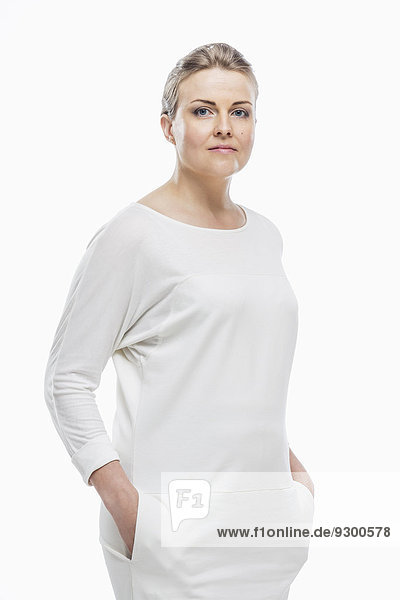 Porträt einer selbstbewussten Frau mit Händen in den Taschen vor weißem Hintergrund