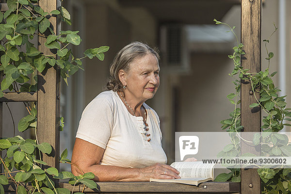 Senior woman holding book while looking away in balcony