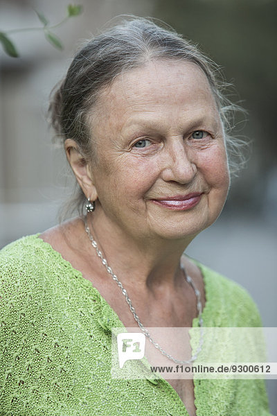 Nahaufnahme des Porträts einer älteren Frau  die im Freien lächelt.