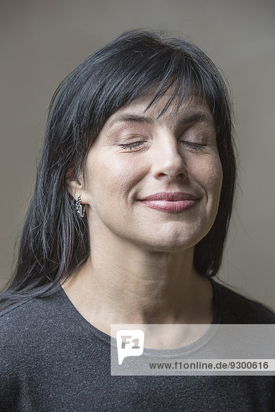 Lächelnde reife Frau mit geschlossenen Augen vor grauem Hintergrund