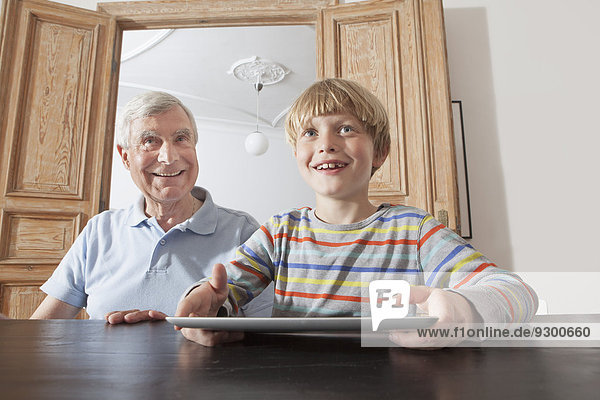 Glücklicher älterer Mann sitzend durch Enkel mit digitalem Tablett zu Hause