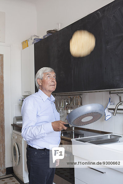 Senior Mann wirft Pfannkuchen auf Bratpfanne in der Küche zu Hause