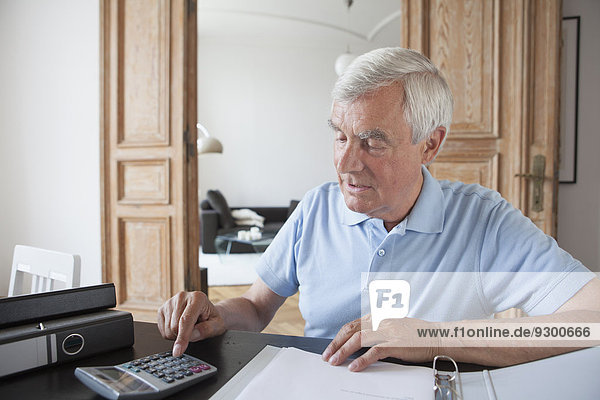 Senior man using calculator to calculate home finances at table