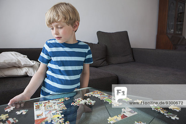 Junge löst Puzzle auf Glastisch im Wohnzimmer zu Hause