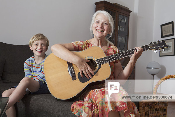 Portrait of boy sitting with grandmother playing guitar on sofa at home