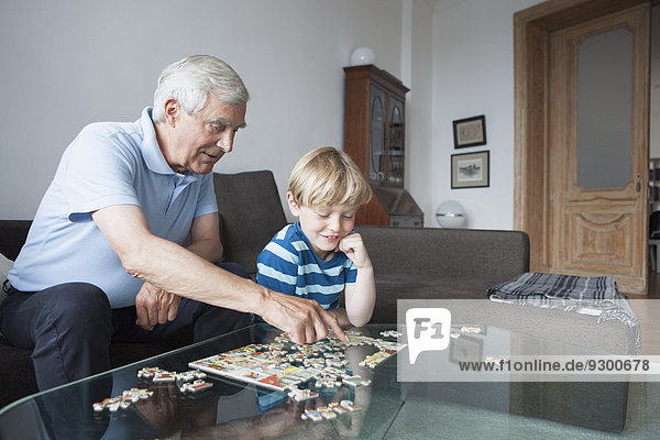 Großvater löst Puzzle mit Enkel im Wohnzimmer zu Hause