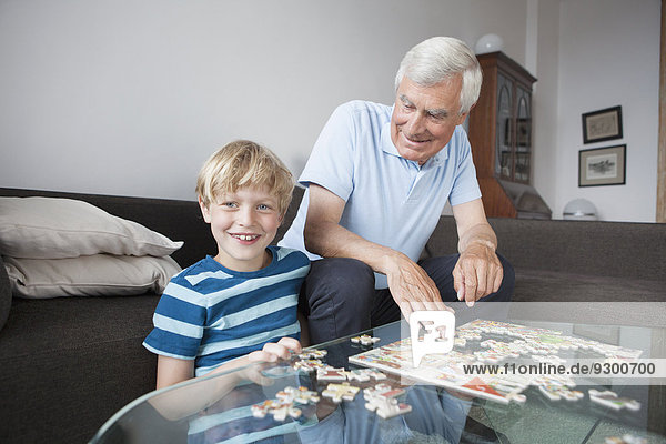 Portrait of happy grandson solving jigsaw puzzle with grandfather in living room at home