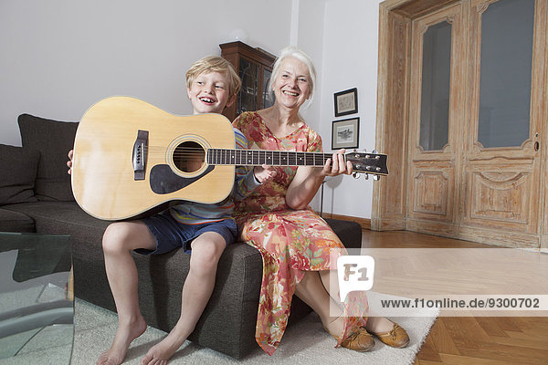 Happy grandson and grandmother with guitar sitting on sofa at home