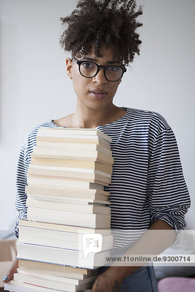 Porträt einer selbstbewussten jungen Frau mit Bücherstapel zu Hause