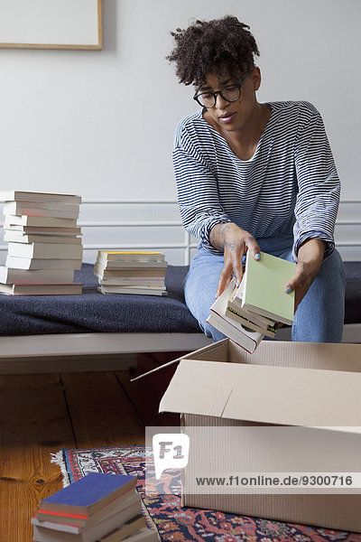Junge Frau beim Verpacken von Büchern im Karton zu Hause