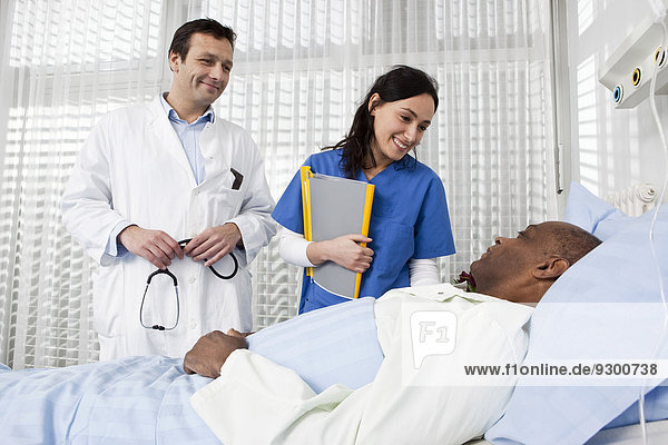 A doctor and nurse talking to a patient lying in a hospital bed