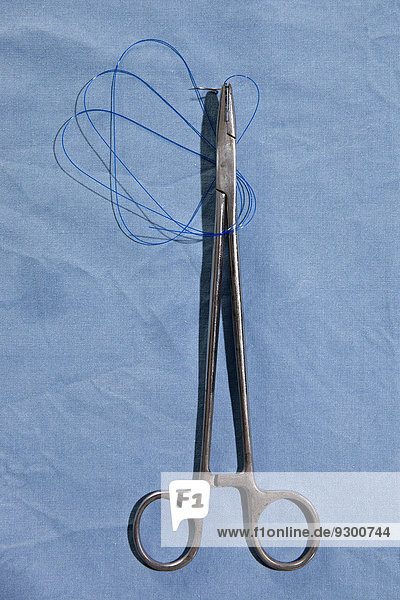 Eine chirurgische Schere  die eine Nähnadel und einen Faden direkt darüber hält.