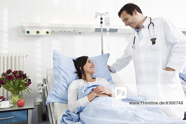 A doctor talking to a smiling patient lying in a hospital bed